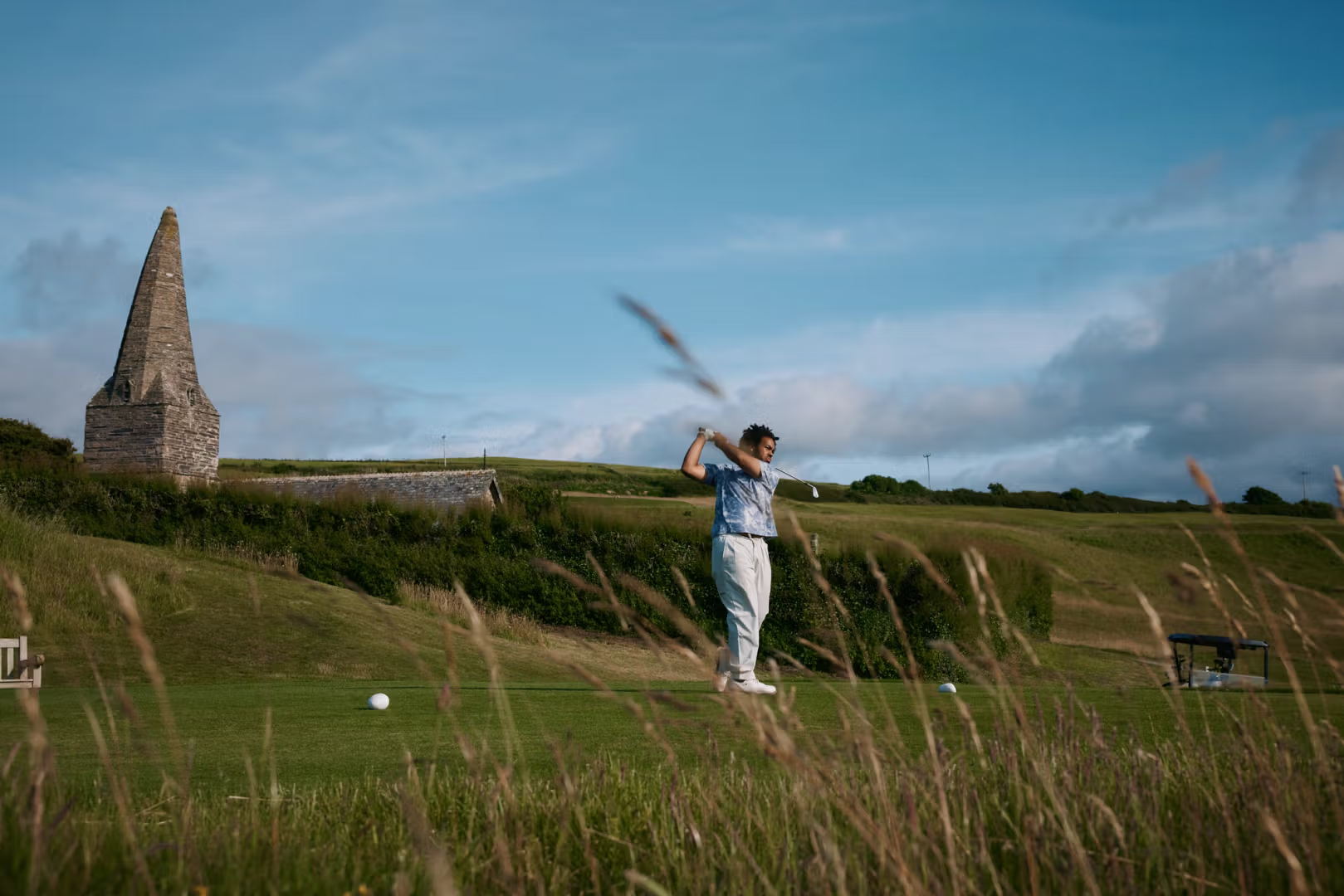Golfer swinging at a historic course with stone tower